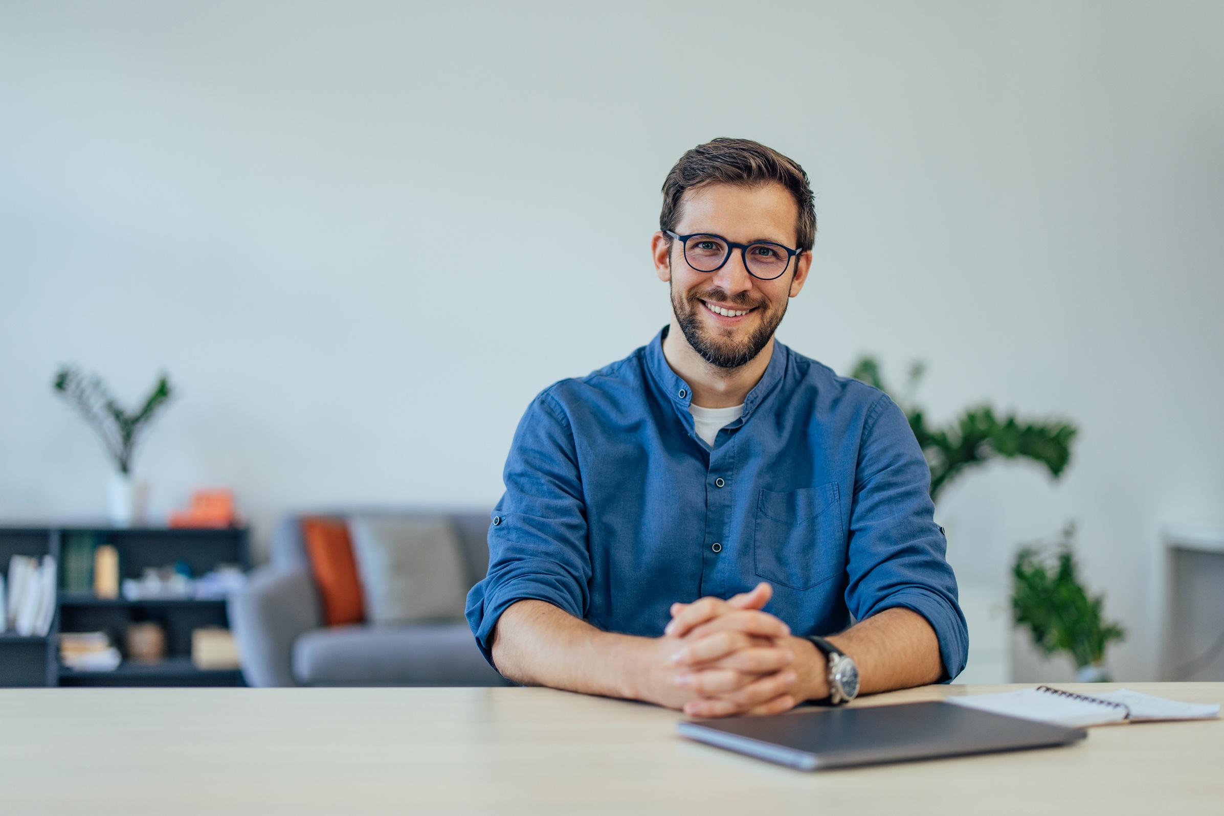 Smiling Professional in Modern Office with Laptop and Notebook on Desk Smiling Professional In Modern Office With Laptop U3KEAEN
